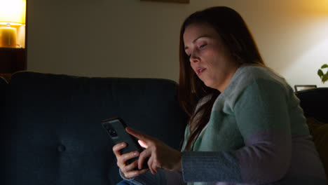 Woman-Sitting-On-Sofa-At-Home-At-Night-Streaming-Or-Watching-Movie-Or-Show-On-Laptop-And-Scrolling-Internet-On-Phone-9